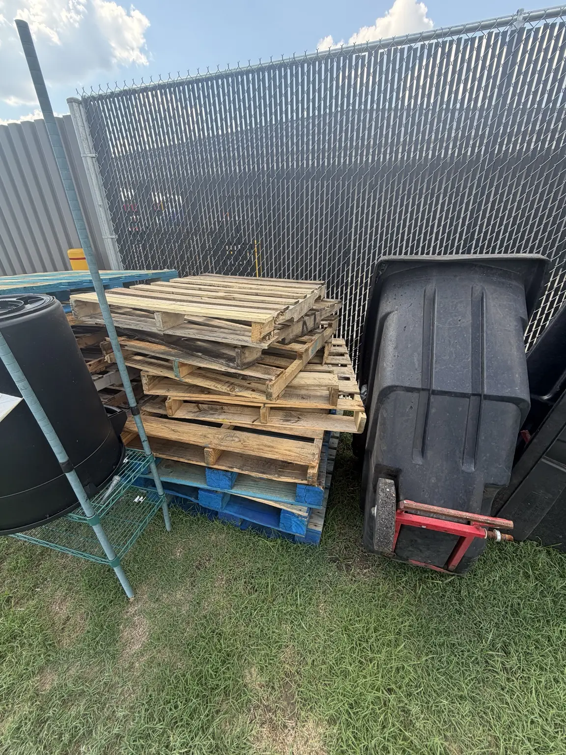 Wood pallets and bulky waste stacked beside a commercial dumpster enclosure