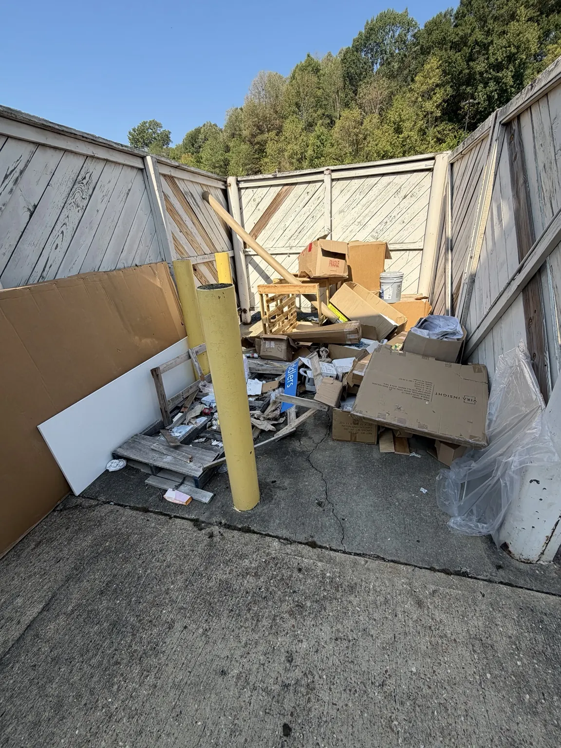 Cardboard boxes, broken wood and packaging cluttering a fenced commercial area in Frisco