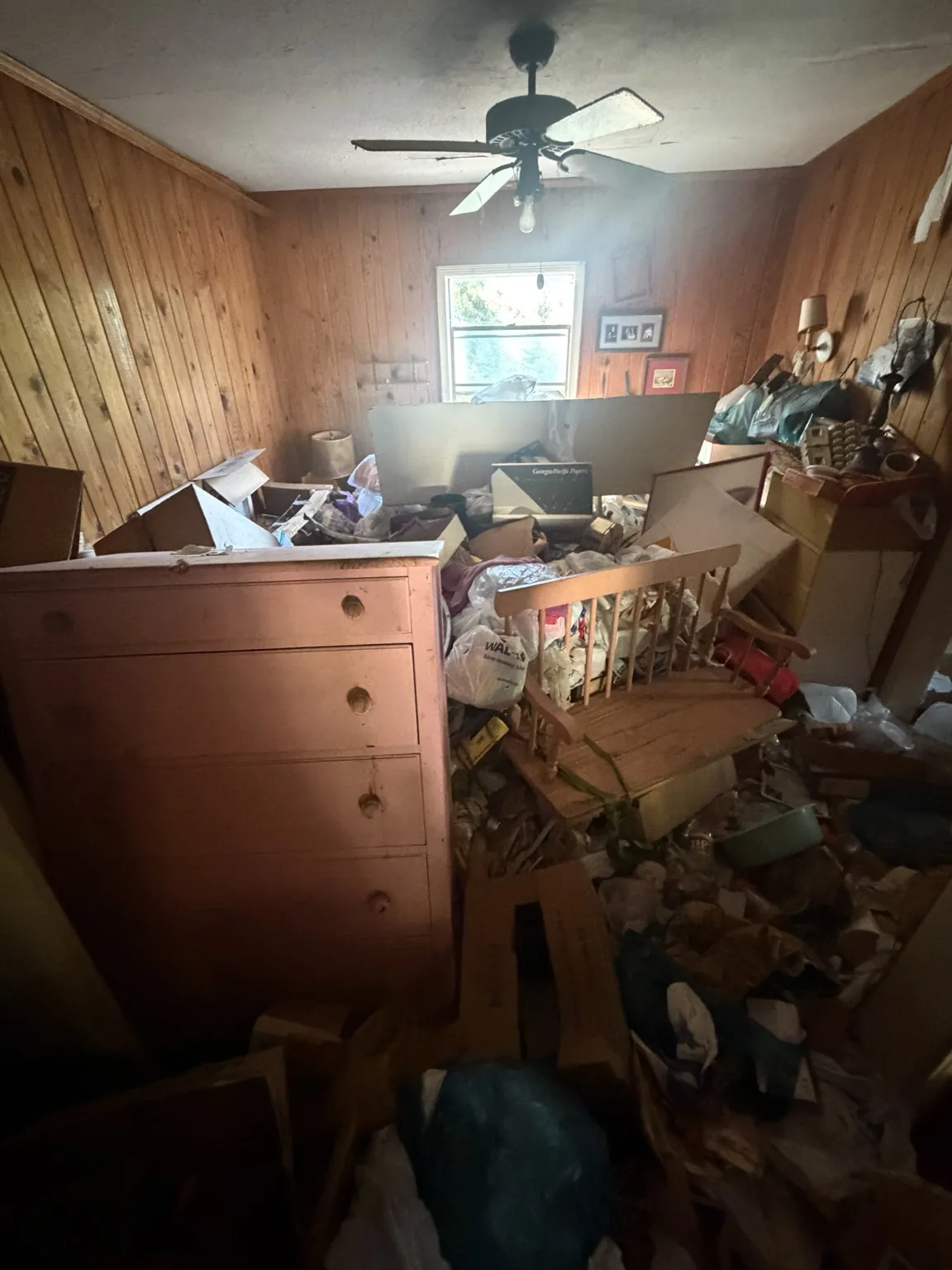 Wood-paneled room containing a dresser and piled household belongings