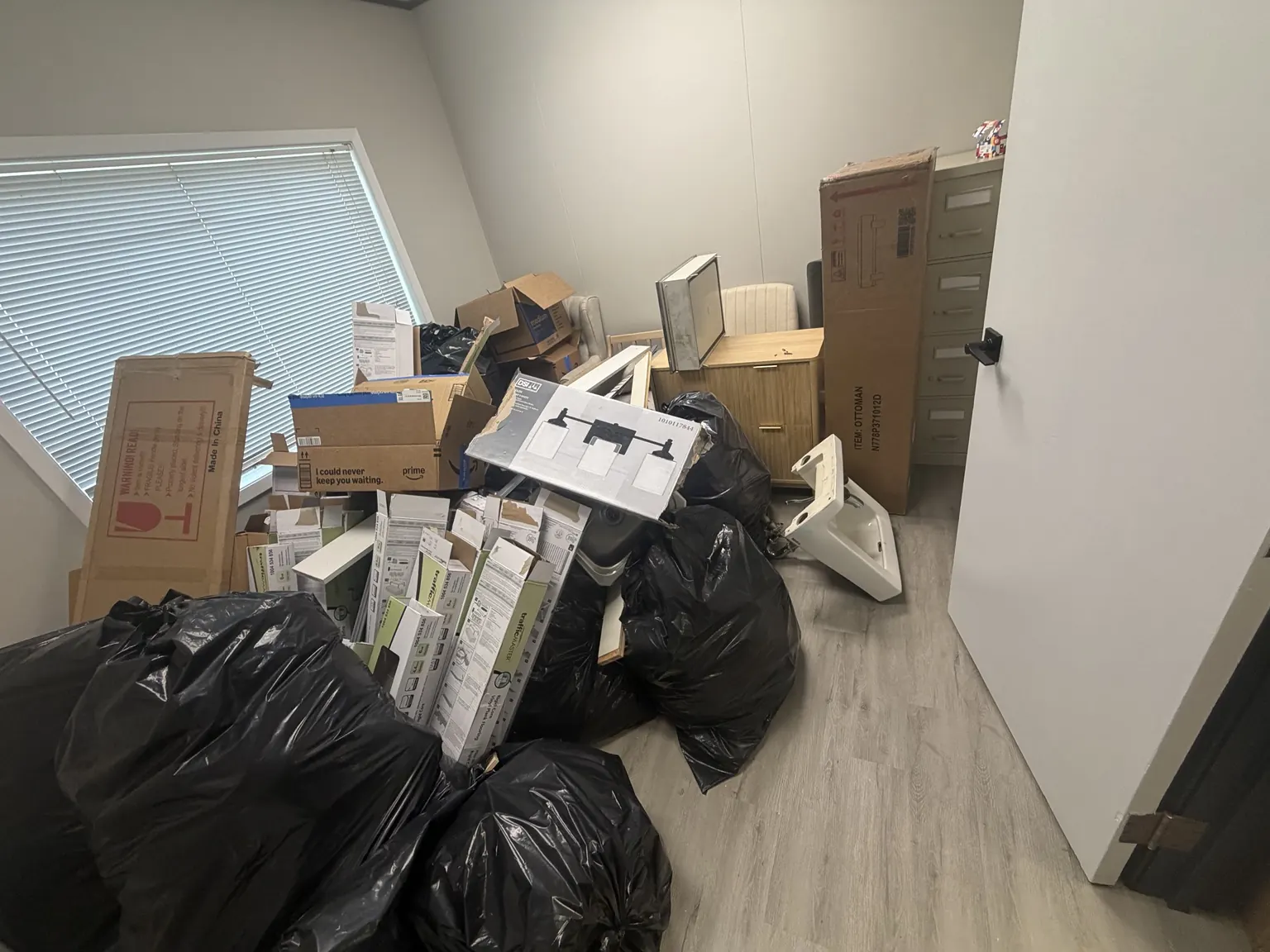 Wider view of the office before removal, with boxes, bagged items and panels across the room