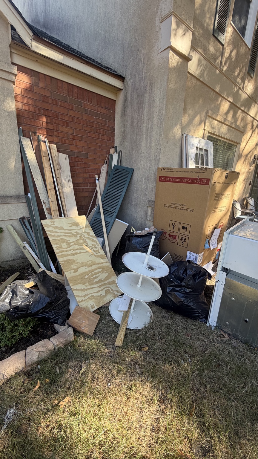 Mixed outdoor clutter and boards beside a home before pickup